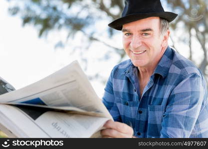 Senior gentleman reading newspaper in park. Enjoying reading