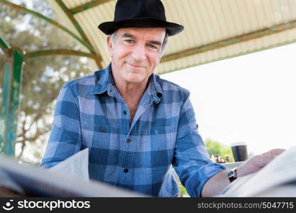 Senior gentleman reading newspaper in park. Enjoying reading