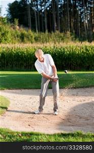 Senior golf player chipping his ball out of a sand trap, ball in motion and lots of sand frozen (short shutter speed)