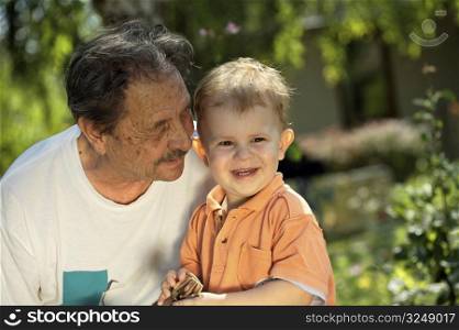 Senior grandfather and two years old grandson play together in the garden, at home.