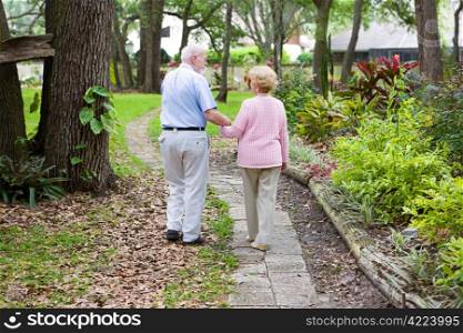 Senior husband and wife holding hands and walking down a garden path.