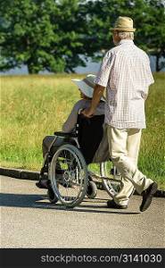 Senior husband pushing wife&acute;s wheelchair in park