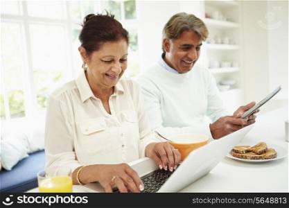 Senior Indian Couple Using Laptop And Digital Tablet At Home