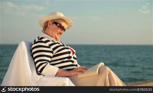 Senior lady relaxing on the seacoast, reading book