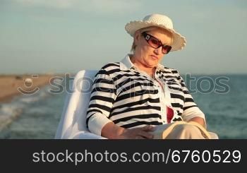 Senior lady relaxing with good book on the seacoast at sunset