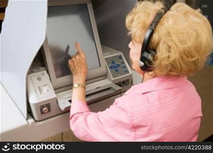Senior lady using headphones for hearing impaired and voting on touch screen machine.