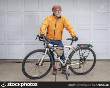 senior make cyclist standing with his touring bike in a driveway