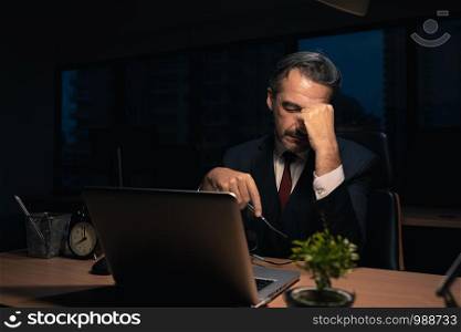 Senior male businessman in executive positions Serious And tired from overtime at the office at night , The manager is working with fatigue at night.