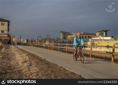 senior male cyclist is riding a gravel bike on a bike trail through city of Fort Collins in northern Colorado, cold winter afternoon