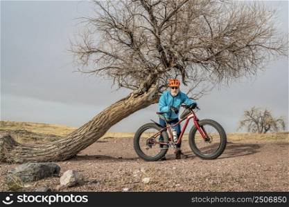senior male cyclist with a fat mountain bike in northern Colorado prairie, early spring scenery in Soapstone Prairie Natural Area near Fort Collins