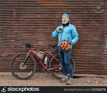 senior male cyclist with a gravel bike is taking a break at old corrugated metal barn in Colorado countryside