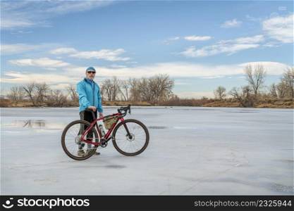 senior male cyclist with a gravel bike on a frozen lake in winter or early spring - Arapaho Bend Natural Area in Fort Collins, Colorado