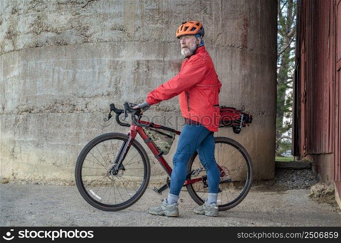 senior male cyclist with a gravel bike taking a break at old barn in Colorado coutryside