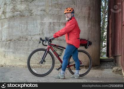 senior male cyclist with a gravel bike taking a break at old barn in Colorado coutryside