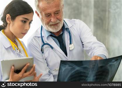 Senior male doctor looking at x ray film of patient chest injury while working with another doctor at the hospital. Medical healthcare staff and doctor service.