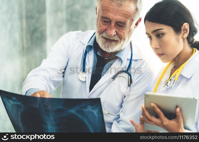 Senior male doctor looking at x ray film of patient chest injury while working with another doctor at the hospital. Medical healthcare staff and doctor service.