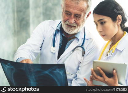 Senior male doctor looking at x ray film of patient chest injury while working with another doctor at the hospital. Medical healthcare staff and doctor service.