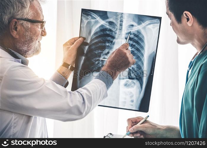Senior male doctor looking at x ray film of patient chest injury while working with another doctor at the hospital. Medical healthcare staff and doctor service.. Doctors working with x ray film of patient chest.