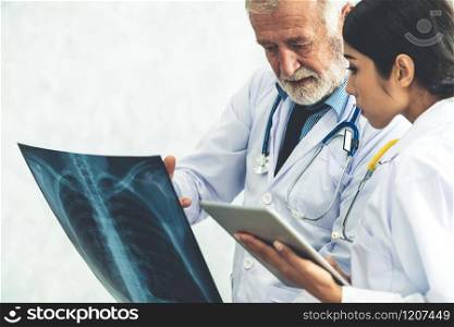 Senior male doctor looking at x ray film of patient chest injury while working with another doctor at the hospital. Medical healthcare staff and doctor service.. Doctors working with x ray film of patient chest.