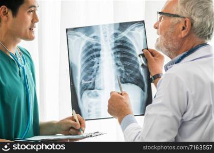 Senior male doctor looking at x ray film of patient chest injury while working with another doctor at the hospital. Medical healthcare staff and doctor service.