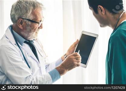 Senior male doctor using tablet computer while discussing with another doctor at the hospital. Medical healthcare staff and doctor service.. Doctors working with tablet computer at hospital.