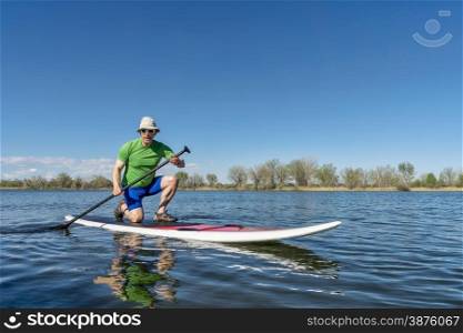 Senior male exercising on stand up paddling (SUP) board. Early spring on a calm lake in Fort Collins, Colorado..