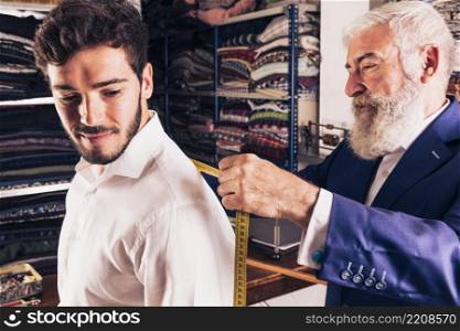 senior male fashion designer taking measurement his customer shop