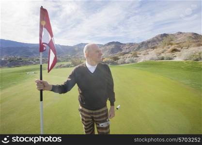 Senior male golfer looking away while holding flag and putter at golf course