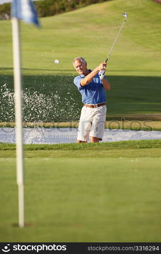 Senior Male Golfer Playing Bunker Shot On Golf Course