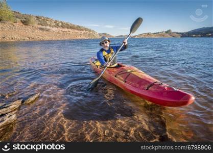 senior male is paddling colorful river kayak on a calm lake Horsetooth Reservoir) - recreation concept