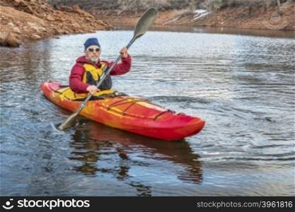 senior male is paddling colorful river kayak on a calm lake - recreation concept