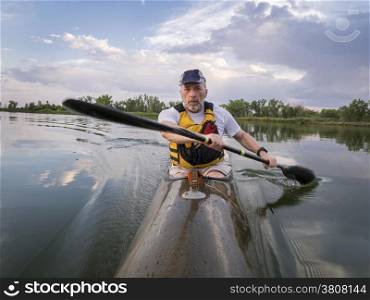 senior male is paddling racing sea kayak on a calm lake with storm clouds in background, Fort Collins, Colorado