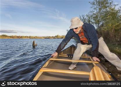 senior male launching canoe for morning paddling, on a lake Riverbend Ponds Natural Area, Fort Collins, Colorado