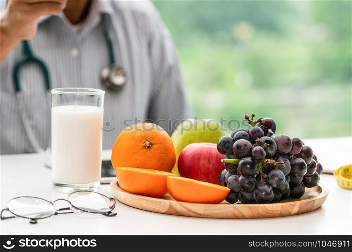 Senior male nutritionist doctor working on desk with healthy food fruits and milk on table in the hospital office. Dieting and well eating menu concept.