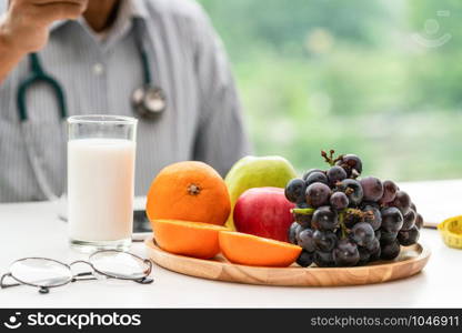 Senior male nutritionist doctor working on desk with healthy food fruits and milk on table in the hospital office. Dieting and well eating menu concept.