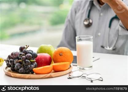Senior male nutritionist doctor working on desk with healthy food fruits and milk on table in the hospital office. Dieting and well eating menu concept.