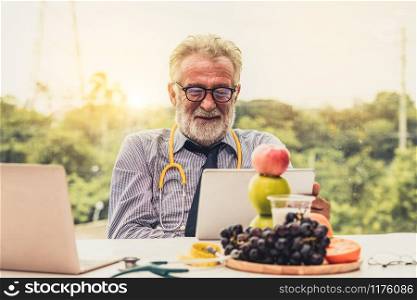 Senior male nutritionist doctor working with laptop computer on table in the hospital office. Dieting and healthy eating concept.