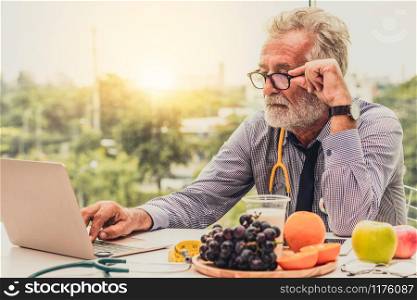 Senior male nutritionist doctor working with laptop computer on table in the hospital office. Dieting and healthy eating concept.