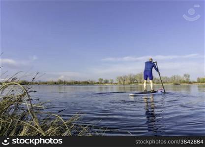 Senior male on stand up paddling (SUP) board. Early spring on calm lake in Fort Collins, Colorado..