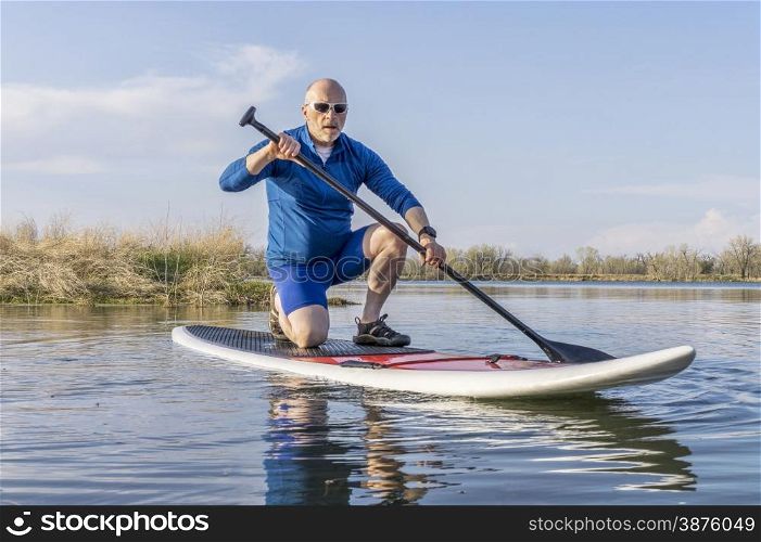 Senior male on stand up paddling (SUP) board. Early spring on calm lake in Colorado.