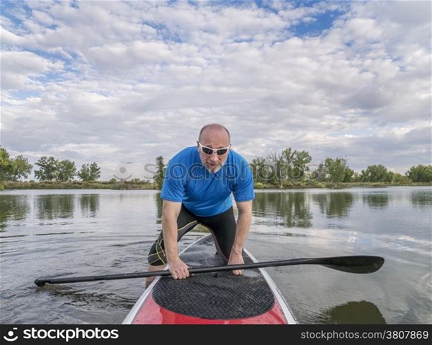 senior male paddler boarding a stand up paddleboard (SUP), calm lake in Colorado, late summer