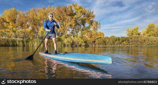 Senior male paddler enjoys workout on his racing stand up paddleboard on a lake in fall colors in northern Colorado