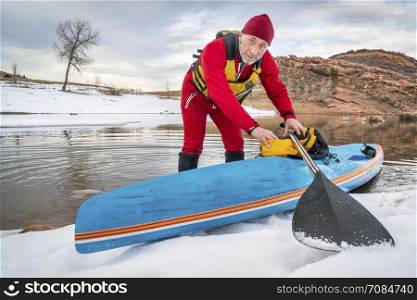 senior male paddler in drysuit and a racing stand up paddleboard on lake in Colorado, winter scenery