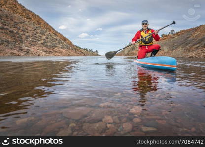 senior male paddler in drysuit is enjoying stand up paddling on lake in Colorado, winter scenery with some ice