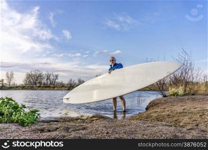 senior male paddler is launching his paddleboard on a lake, early spring in Colorado
