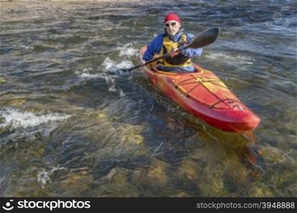 senior male paddler is paddling whitewater kayak on a turbulent river