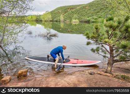senior male paddler launching his red SUP paddleboard at a rocky lake shore (Horsetooth Reservoir, Fort Collins, Colorado)