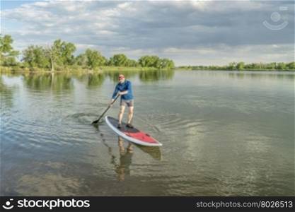 senior male paddler on a paddleboard, lake in northern Colorado with an early summer scenery