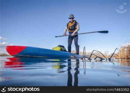 senior male paddler on a stand up paddleboard, a calm lake in Colorado, winter or early spring scenery, low angle action camera view, recreation, fitness and training concept