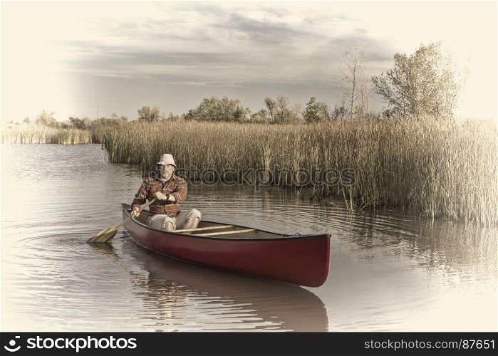 senior male paddler paddling a canoe on a calm lake, retro opalotype toning